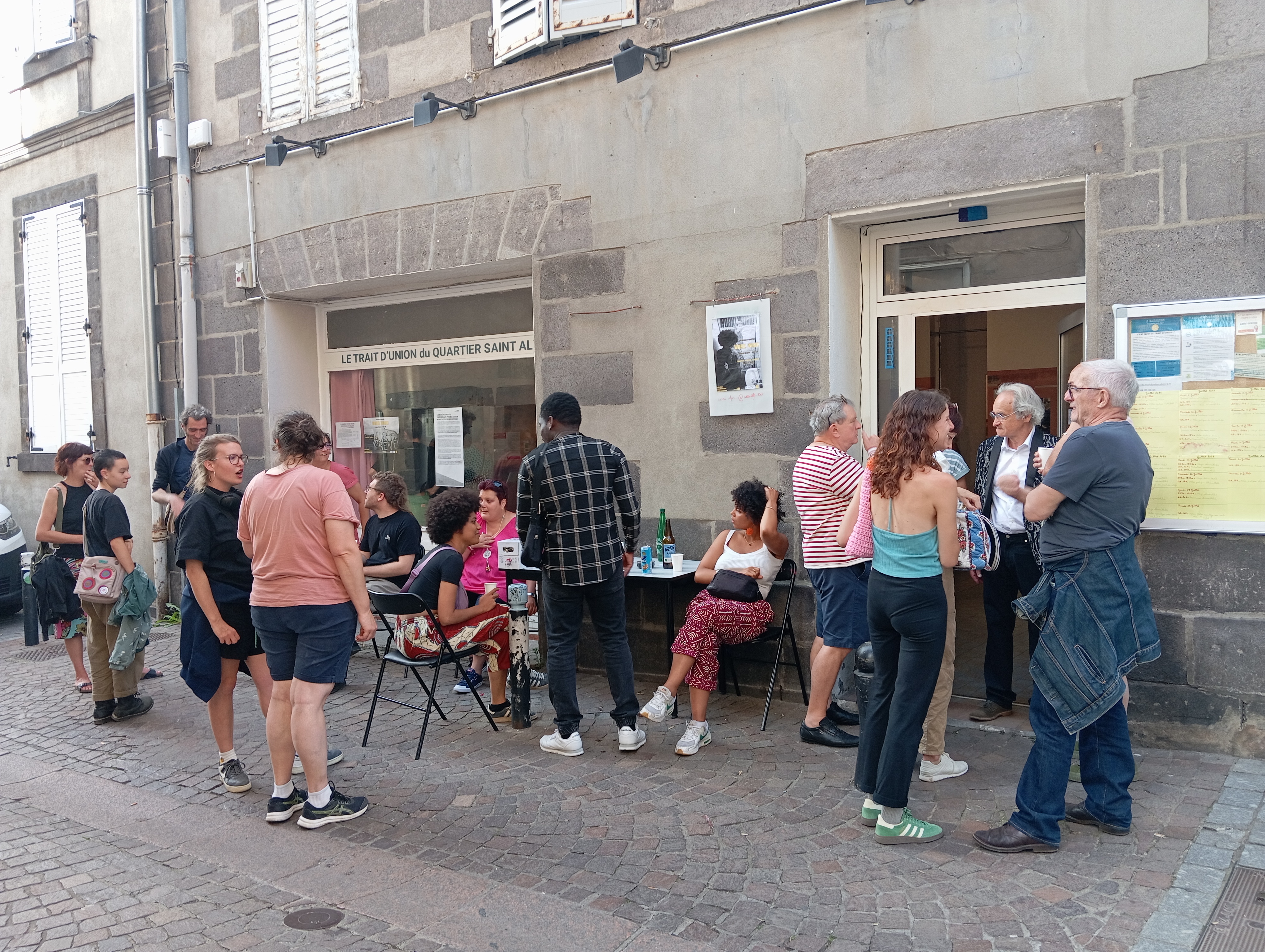 Photo du local du Trait d'Union, depuis la rue Sainte-Claire, avec des personnes qui discutent dehors.