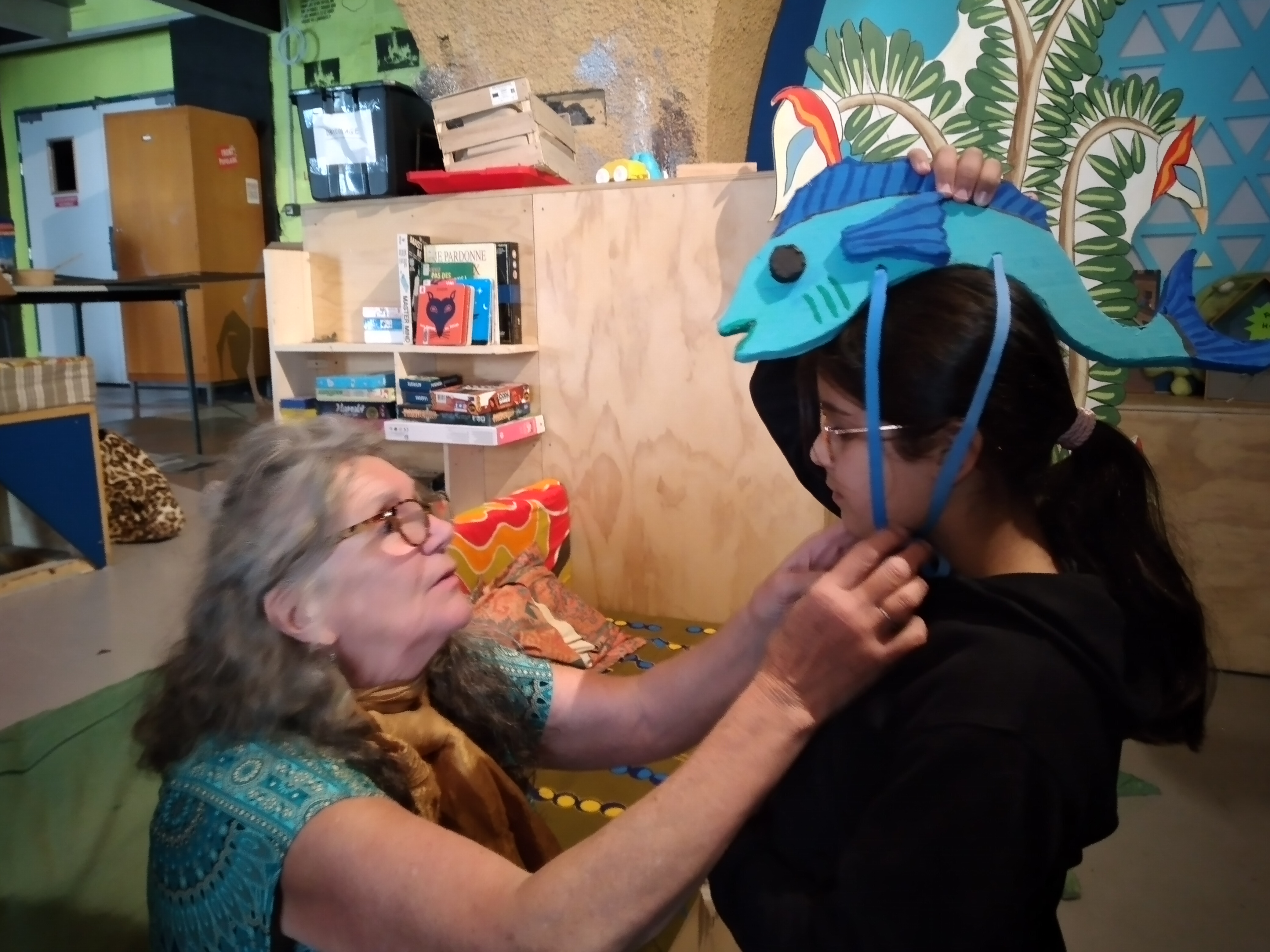 Une femme accroche un poisson bleu sur la tête d'une enfant.