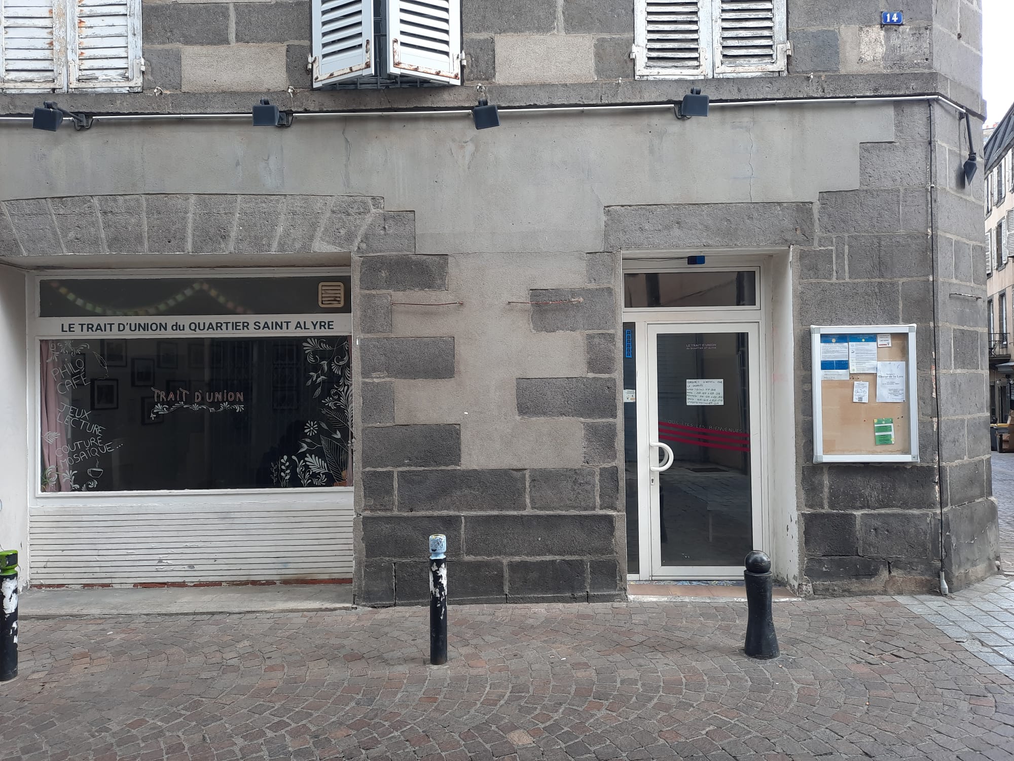 photo de la façade du Trait d'Union du quartier Saint-Alyre, depuis la rue Sainte-Claire : vitrine à gauche, porte d'entrée et panneau d'affichage à droite